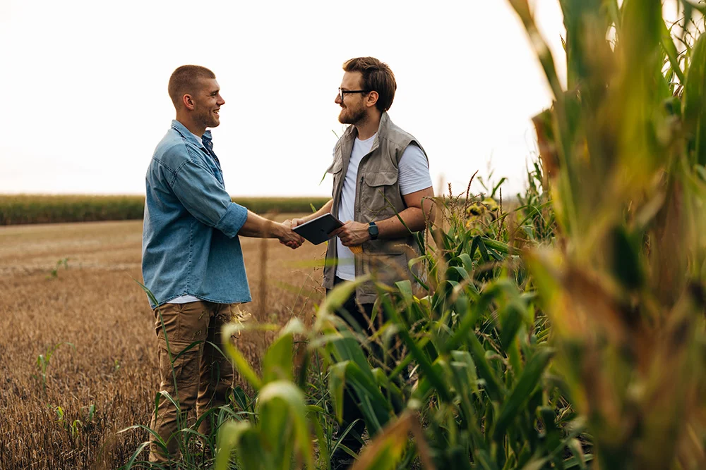 A farmer and a businessman shaking hands in a corn field